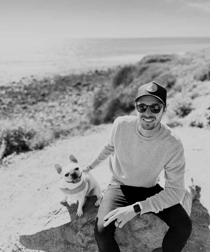 Man and dog sitting on a rocky trail with ocean view